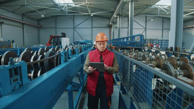 Professional asian industry engineer man wearing safety uniform and hard hat walk use tablet computer checks production processes in factory. Look around. Inspector in warehouse.