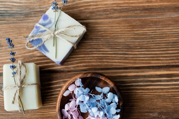 Top view of flowers in bowl near handmade soap bars on wooden surface.