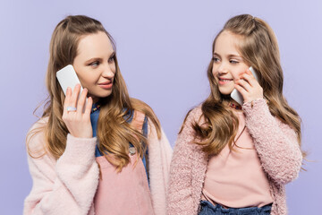 happy mother and daughter talking on mobile phones isolated on purple.
