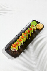 Modern asian food - sushi roll with avocado and tuna on black plate on white concrete background.  Maki roll with avocado outside, tuna and cheese inside. Avocado maki. Fusion sushi menu.