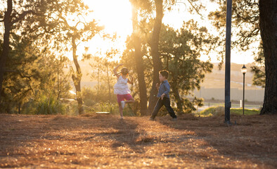 Niños felices amigos hermanos jugando corriendo brincando saltando disfrutando de un atardecer en un parque al aire libre - obrazy, fototapety, plakaty