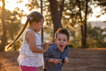 Niños felices amigos hermanos jugando corriendo brincando saltando disfrutando de un atardecer en un parque al aire libre - obrazy, fototapety, plakaty