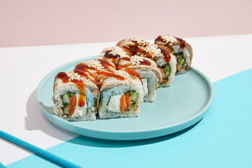Canada Maki roll with eel on modern coloured background. Sushi roll with salmon, cheese, cucumber inside, eel and unagi sauce outside. Unagi maki sushi in minimal style. Japanese menu concept.