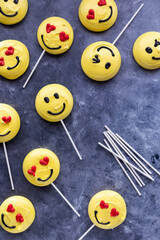 Several smiley face emoji merengue cookies with lollipop sticks.