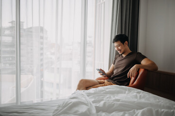 Asian man feels happy with his phone result while on vacation in the hotel.
