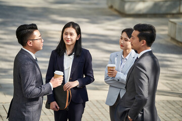 group of four asian business people men and women standing chatting talking outdoors on street