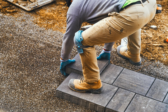 Landscaping paver worker laying paving stones on sandy ground of construction driveway site in spring. Landscape business and contractor installation work background.