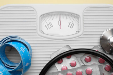 Scales with weight loss pills, measuring tape, and stethoscope, closeup
