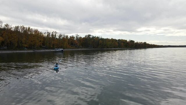Young woman sitting in a small blue kayak paddling over Buffalo Lake on a cloudy autumn day. Aerial parallax shot