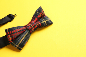 Stylish tartan bow tie on yellow background, closeup. Space for text