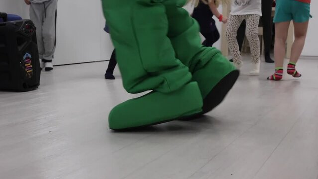 Under loud cheerful music sounding from music column children perform different movements according task of presenter. Animator in green fixie costume dances with children loud fast music from speaker