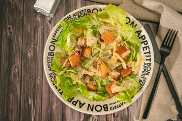 Exquisite traditional Caesar salad of lettuce, toasted bread and fine Parmesan cheese with a garlic aioli and olive oil in a bowl that says Bon Appetite in French on rustic table.