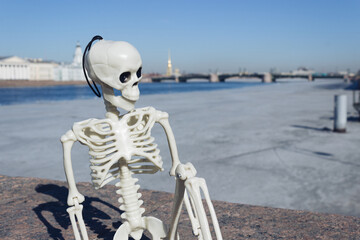Obraz na płótnie Canvas A toy skeleton of a man sits on a granite parapet against the background of the Neva River in St. Petersburg, Russia
