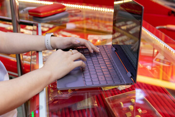 A gold shop employee uses a laptop. Check daily sales