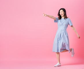 Full length image of young Asian woman wearing blue dress on pink background