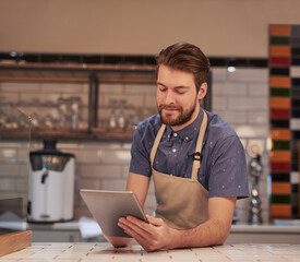 Sending out special offers to all my existing customers. Shot of a young man using a digital tablet while working in a coffee shop.