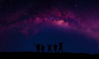 A group of people are happily standing next to the Milky Way galaxy pointing at a bright star.