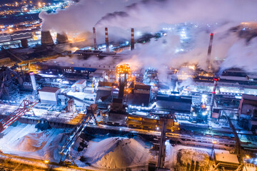 Aerial view of steel plant at night with smokestacks and fire blazing out of the pipe. Industrial panoramic landmark with blast furnance of metallurgical production. Concept of environmental pollution