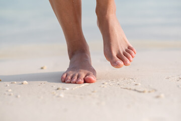 Fototapeta na wymiar Closeup image of woman with barefoot while walking on the white beach and the sea