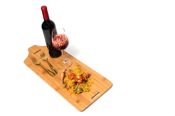 Traditional paella rice from Valencia Spain, made with saffron shellfish, shrimp and vegetables served on a wooden board accompanied by red wine and a glass of clericot on a white background
