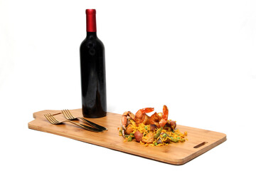 Traditional paella rice from Valencia Spain, made with saffron shellfish, shrimp and vegetables served on a wooden board accompanied by red wine and a glass of clericot on a white background
