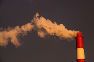 steam smoke from an industrial red white chimney against a dark sky, in the light of sunset