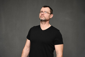 Adult caucasian man in glasses portrait looking up with a smile on a gray background