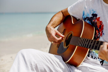 Close-up of a man playing a classical guitar while sitting on the beach in summer. Lifestyle, rest,...