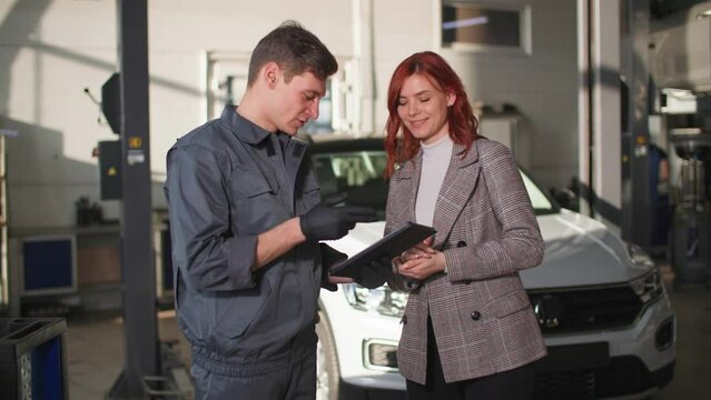 service center, a young male mechanic shows a satisfied female client on a tablet technical condition of car during vehicle technical inspection
