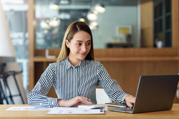 Beautiful Asian business woman sitting working on laptop in office.