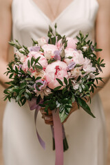A luxurious wedding bouquet with pink peonies in the hands of the bride