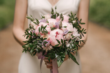 A luxurious wedding bouquet with pink peonies in the hands of the bride