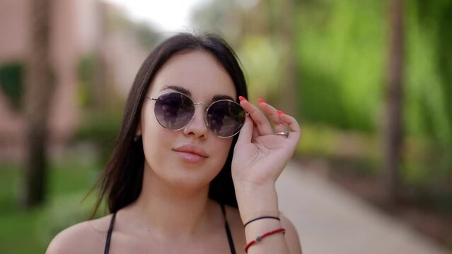 sexy young woman with full lips is walking in summer, correcting sunglasses and looking at camera