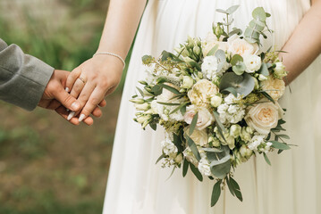 Obraz na płótnie Canvas A luxurious wedding bouquet with white roses in the hands of the bride and groom
