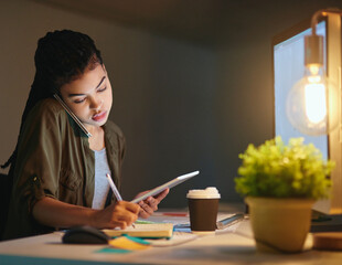 Its always good to take notes. Shot of a young businesswoman on a call and using a tablet at the...