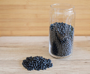 Fototapeta na wymiar Black beans in a clear glass, raw beans in a glass bowl and a spoon on the table. Black beans are good for health. It is a source of protein, fiber, and disease-fighting antioxidants. 