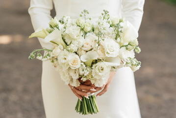 A luxurious wedding bouquet with white roses, carnations and koalas in the hands of the bride