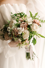 A luxurious wedding bouquet with roses and carnations in the hands of the bride