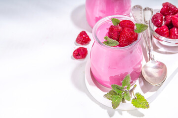 Raspberry panna cotta dessert with fresh raspberries and lemon balm mint leaves. Pink panna cotta in small portion jars on a white background