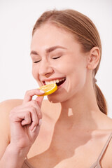 beautiful blonde woman laying on a white wooden background next to slices of lemon, having a slice of lemon on the eyes and smiling