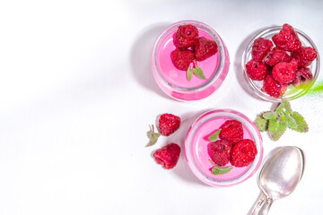 Raspberry panna cotta dessert with fresh raspberries and lemon balm mint leaves. Pink panna cotta in small portion jars on a white background