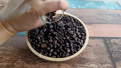Pouring coffee beans from a glass bottle onto a wooden plate.