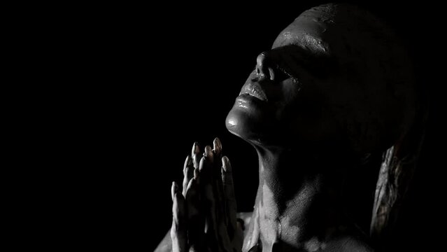beautiful blindfolded woman is covered grey clay is moving slowly in darkness, closeup view of face