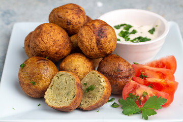 Falafel with hummus on a black round plate with fresh red cherry tomatoes and green parsley on a white table - a traditional dish of Greek and Arabic cuisine