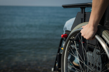 Caucasian woman in a wheelchair on the seashore. Close-up of female hands.