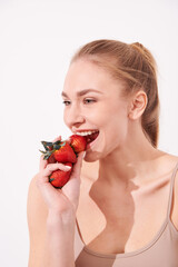 A creative portrait of a beautiful girl holding with one hand a juicy strawberry near her lips with temptation.