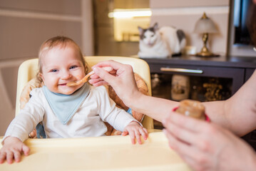 Fototapeta premium Mom feeds a happy baby fruit puree from a spoon. First food