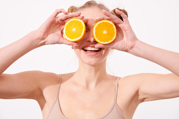 Pretty charming joyful attractive cheerful funny comic positive nude natural pure girl having two pieces of orange, closing one eye, isolated on beige background with copy space for advertisement