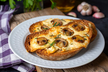 Toasted sandwich from traditional sourdough bread with cheese and brown mushrooms seasoned with rosemary herb on a wooden board, top view