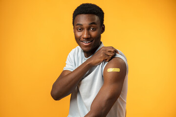 Vaccinated african american man showing his arm against yellow background